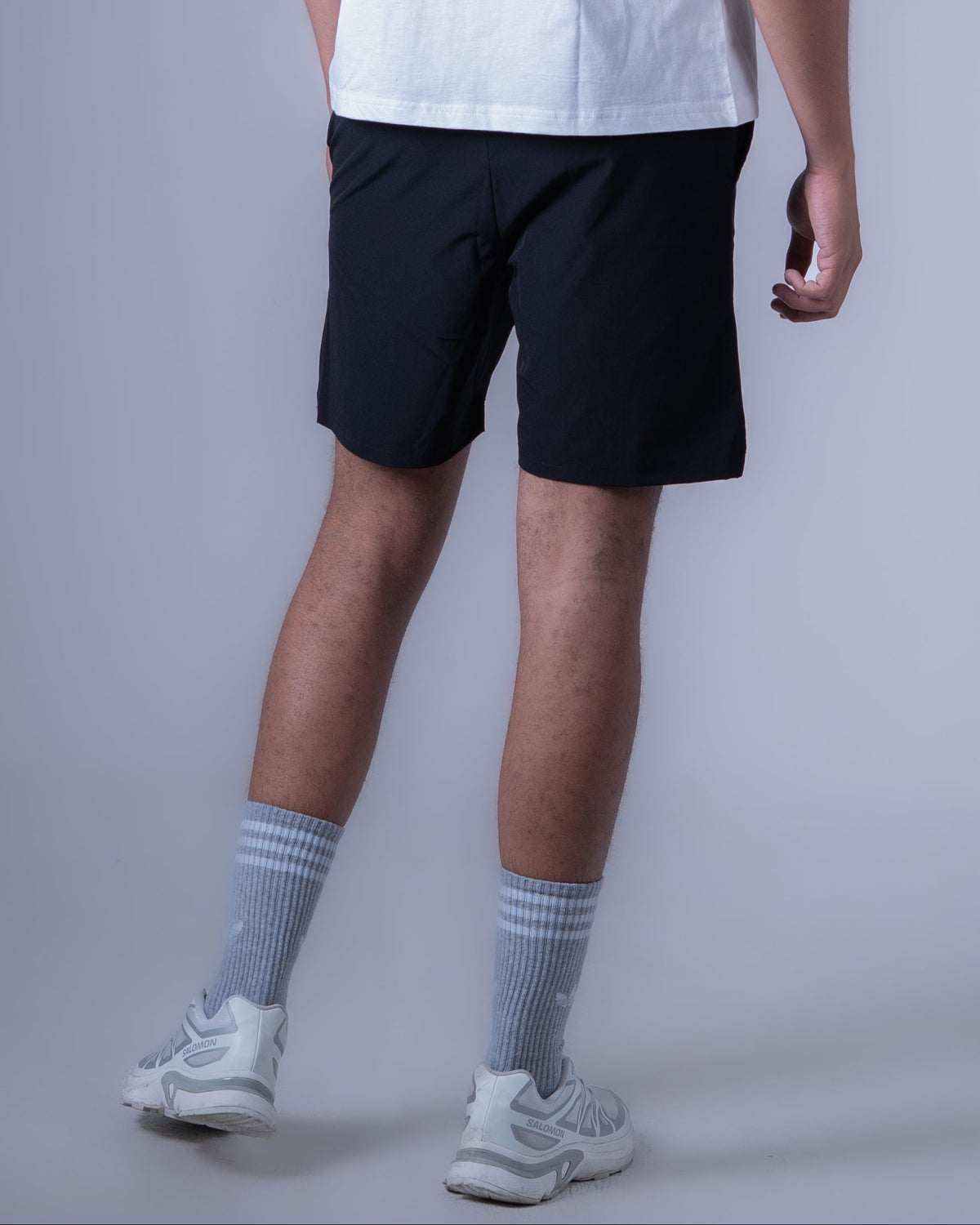 A man wearing a white sleeveless athletic tank top with 'NEXAR' printed vertically on the back, paired with black athletic shorts, gray socks, and white sneakers, shown from a rear three-quarter angle against a gray studio background.